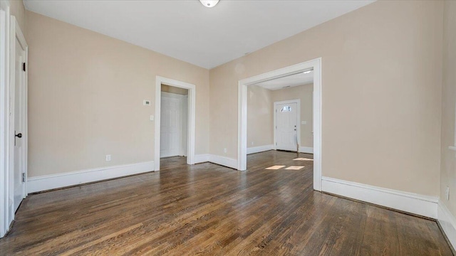 empty room featuring baseboards and dark wood-type flooring