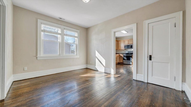 spare room with dark wood-type flooring, visible vents, and baseboards