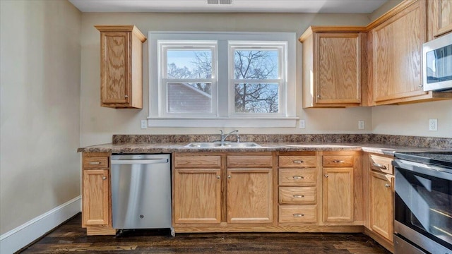 kitchen with stainless steel appliances, a sink, baseboards, light brown cabinetry, and dark countertops