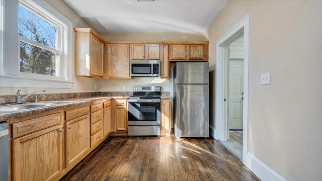 kitchen featuring baseboards, dark countertops, dark wood-type flooring, stainless steel appliances, and a sink