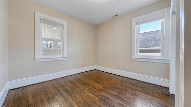 empty room with a wealth of natural light, dark wood-type flooring, visible vents, and baseboards