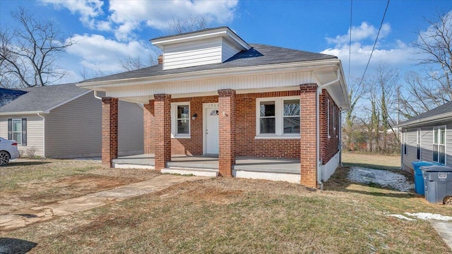 bungalow with a porch, brick siding, and a front lawn