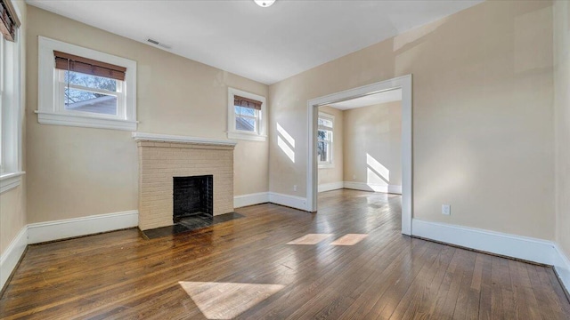 unfurnished living room featuring visible vents, a brick fireplace, dark wood finished floors, and a wealth of natural light