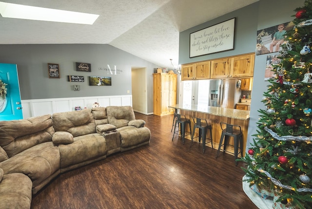 living room with vaulted ceiling with skylight, dark wood-type flooring, and a textured ceiling