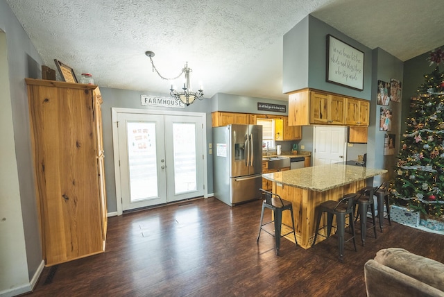 kitchen featuring dark wood-type flooring, stainless steel appliances, light stone counters, a textured ceiling, and a breakfast bar