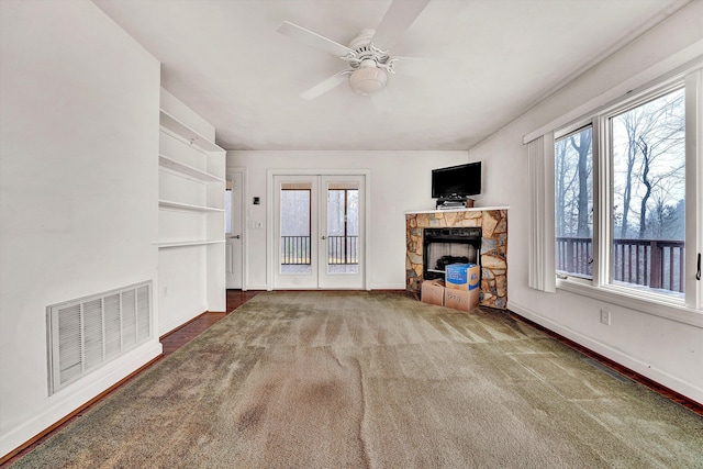 unfurnished living room featuring a fireplace, ceiling fan, french doors, and dark colored carpet