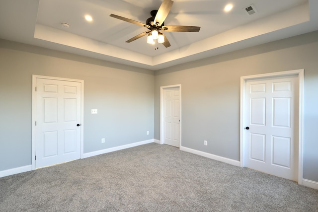 unfurnished bedroom with a tray ceiling, ceiling fan, and carpet flooring