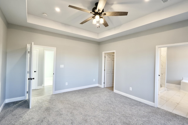 unfurnished bedroom featuring a raised ceiling, light colored carpet, ensuite bath, and ceiling fan