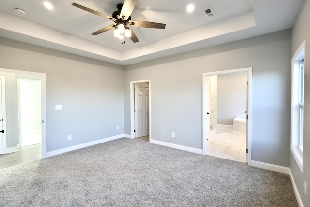 unfurnished bedroom featuring a tray ceiling, connected bathroom, ceiling fan, and light colored carpet