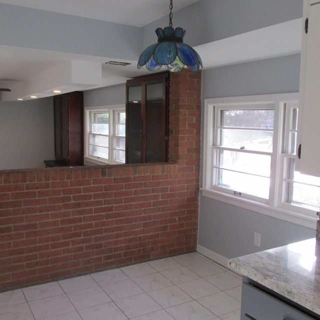 unfurnished dining area with light tile patterned flooring, a healthy amount of sunlight, and brick wall