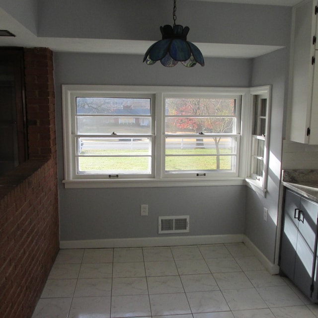 unfurnished dining area with light tile patterned flooring, a wealth of natural light, and brick wall