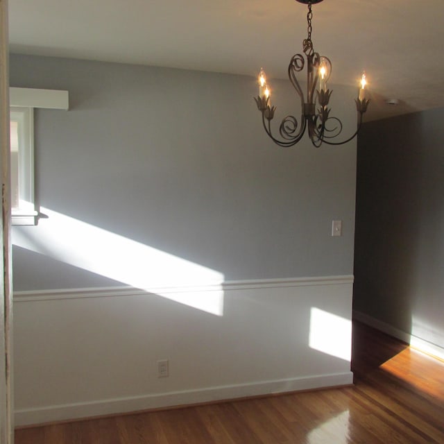 spare room featuring wood-type flooring and an inviting chandelier