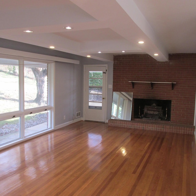 unfurnished living room with wood-type flooring, brick wall, and a brick fireplace