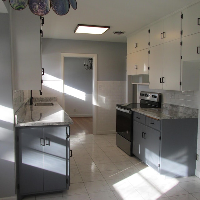 kitchen with stainless steel range with electric stovetop, sink, light tile patterned floors, tasteful backsplash, and white cabinetry