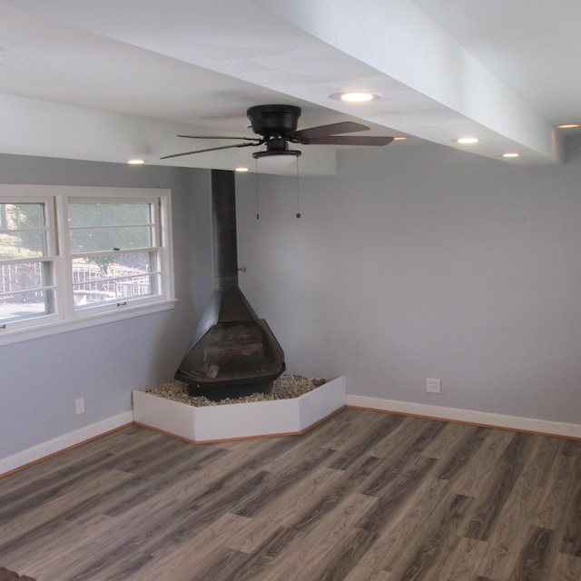 room details featuring wood-type flooring, a wood stove, and ceiling fan