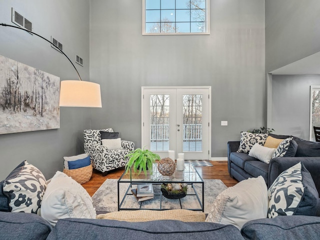 living room featuring a wealth of natural light, french doors, a towering ceiling, and hardwood / wood-style floors