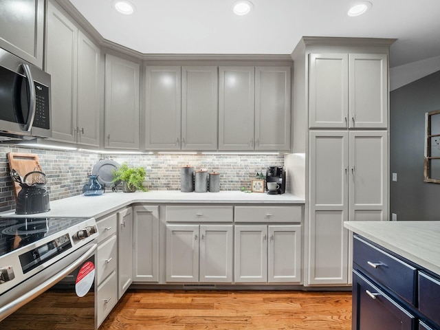 kitchen with backsplash, gray cabinetry, light hardwood / wood-style flooring, and stainless steel appliances