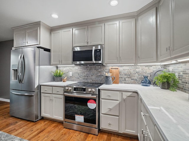 kitchen with tasteful backsplash, light stone countertops, appliances with stainless steel finishes, and light hardwood / wood-style flooring