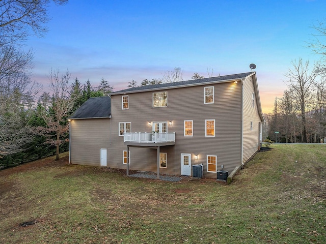 back house at dusk featuring a lawn and cooling unit