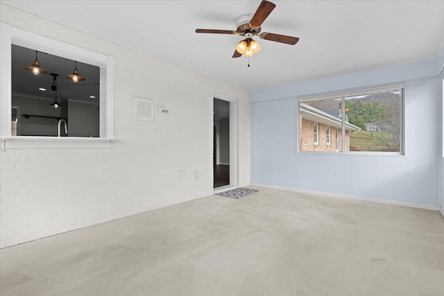 unfurnished room featuring a ceiling fan, carpet, a sink, and brick wall