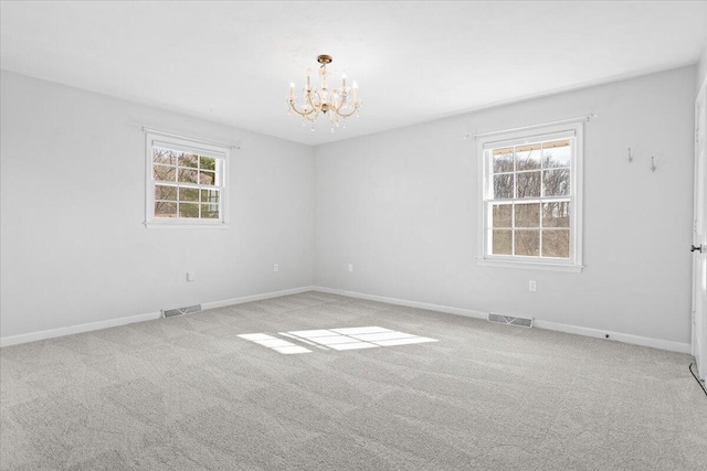 carpeted spare room with a healthy amount of sunlight, visible vents, a notable chandelier, and baseboards