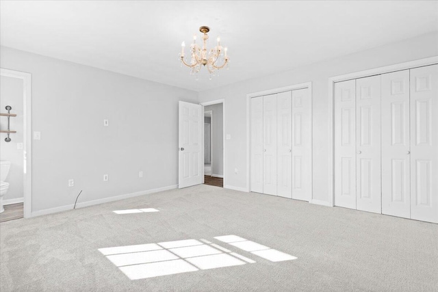 unfurnished bedroom featuring carpet floors, an inviting chandelier, baseboards, and two closets