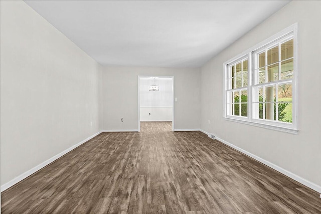 spare room with dark wood finished floors, baseboards, and an inviting chandelier