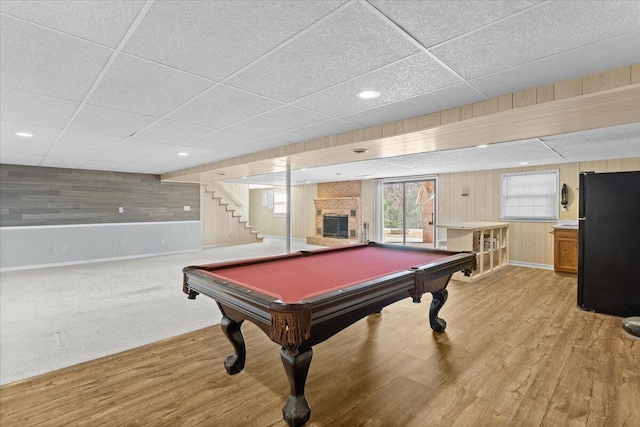 game room featuring light wood-style floors, billiards, a brick fireplace, and wooden walls