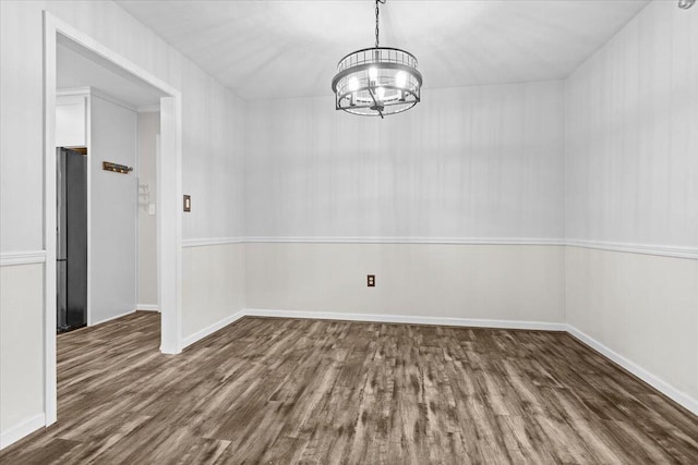 unfurnished dining area featuring a notable chandelier, baseboards, and wood finished floors