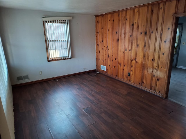 unfurnished room with dark wood-type flooring and wood walls