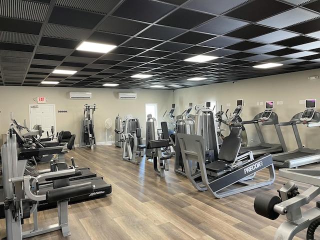 workout area with an AC wall unit, hardwood / wood-style floors, and a drop ceiling