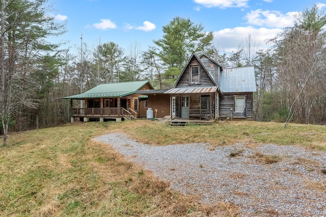 view of front facade with a porch, metal roof, gravel driveway, and a front yard