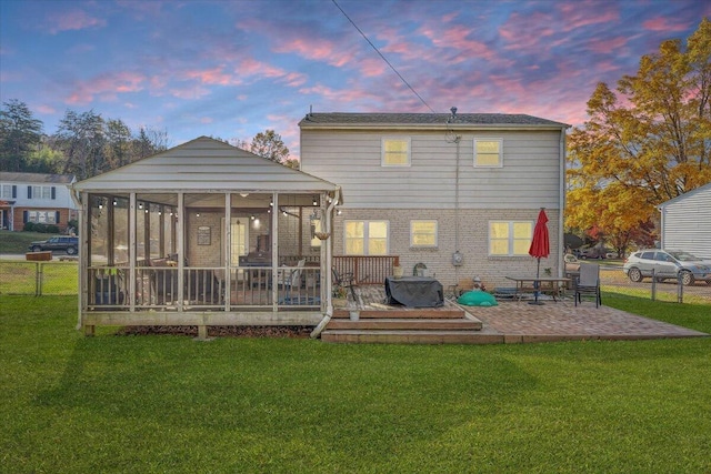 back house at dusk featuring a sunroom, a deck, a yard, and a patio