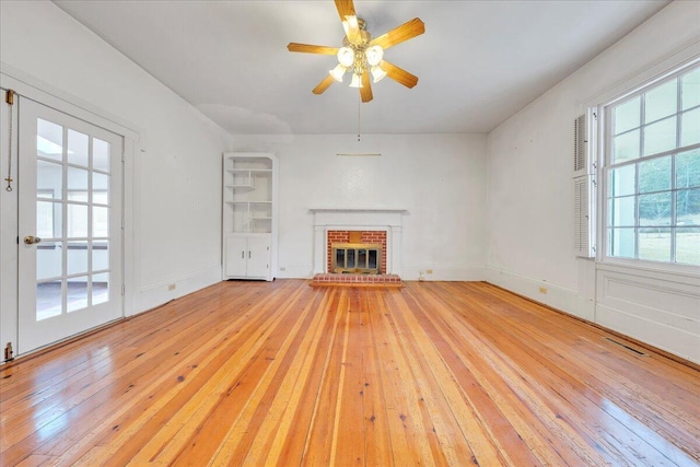 unfurnished living room featuring visible vents, a fireplace, light wood finished floors, baseboards, and ceiling fan