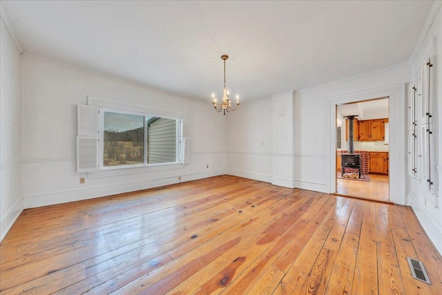 spare room with light wood-type flooring, visible vents, crown molding, a chandelier, and a wood stove