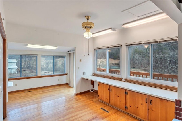 kitchen with visible vents, light wood-style floors, built in desk, and light countertops