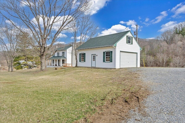 view of front of house featuring an outbuilding, a front lawn, driveway, and roof with shingles