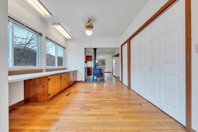 kitchen featuring light wood finished floors, a wood stove, freestanding refrigerator, light countertops, and brown cabinets