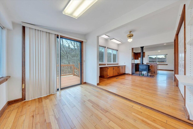 unfurnished living room with baseboards, light wood-style floors, a healthy amount of sunlight, and a wood stove