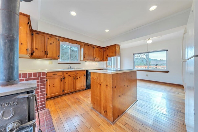 kitchen with light wood-style flooring, ornamental molding, brown cabinetry, light countertops, and a wood stove