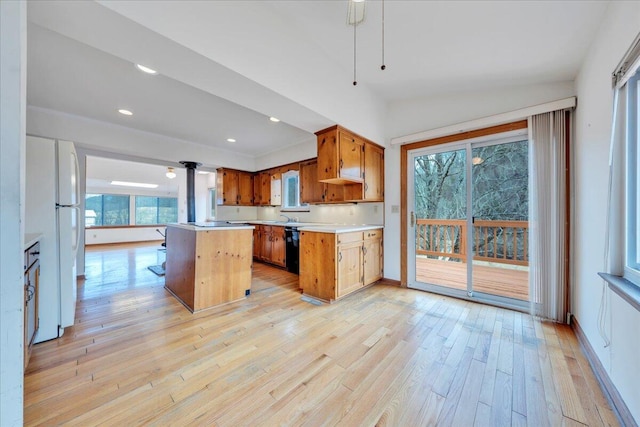 kitchen with black dishwasher, a center island, freestanding refrigerator, light wood-style floors, and light countertops