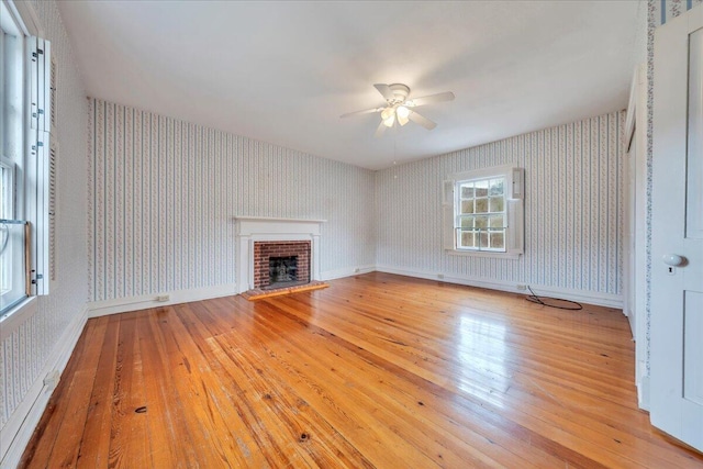 unfurnished living room featuring baseboards, wallpapered walls, a fireplace, ceiling fan, and hardwood / wood-style flooring