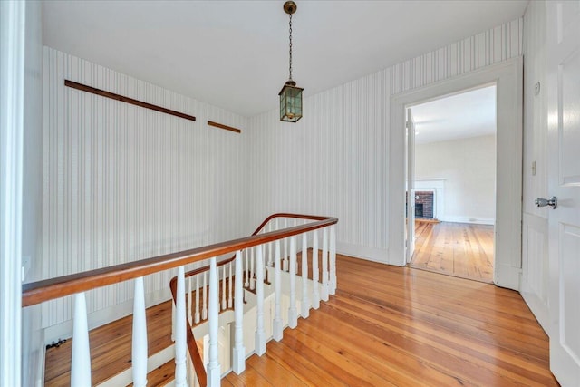 corridor with an upstairs landing, light wood-style flooring, and baseboards