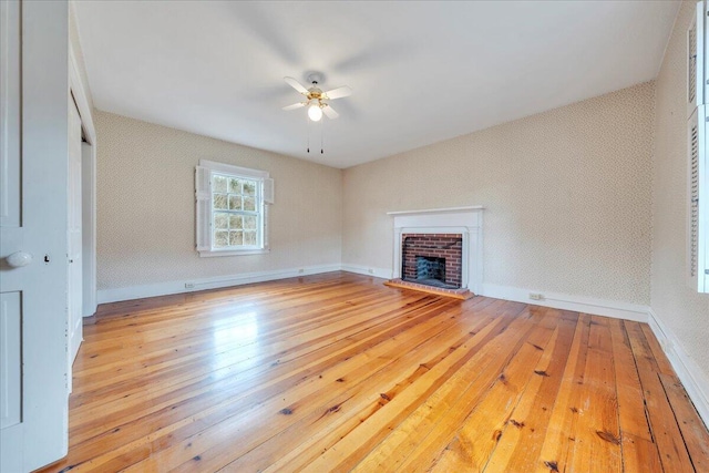 unfurnished living room with hardwood / wood-style floors, wallpapered walls, baseboards, a brick fireplace, and ceiling fan