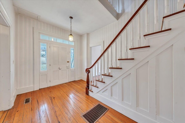 foyer featuring stairway, a decorative wall, light wood-style floors, and visible vents