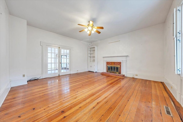 unfurnished living room featuring a ceiling fan, visible vents, light wood-style floors, french doors, and a brick fireplace