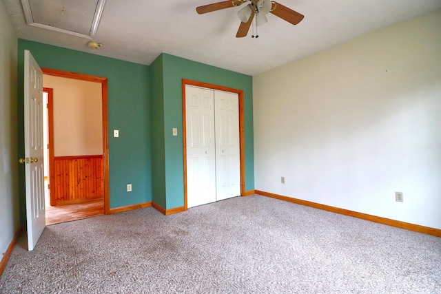 unfurnished bedroom featuring wooden walls, ceiling fan, carpet flooring, and a closet