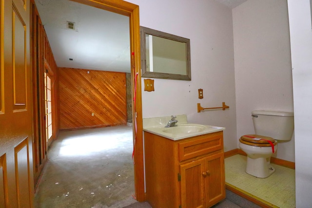 bathroom with toilet, vanity, wooden walls, and concrete floors