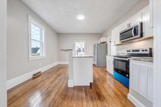 kitchen with dark wood-type flooring, stainless steel appliances, white cabinets, and light stone countertops