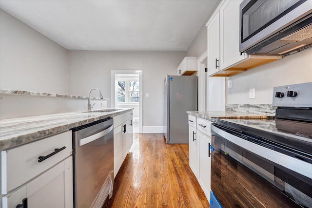 kitchen featuring appliances with stainless steel finishes, white cabinets, light hardwood / wood-style flooring, light stone counters, and sink